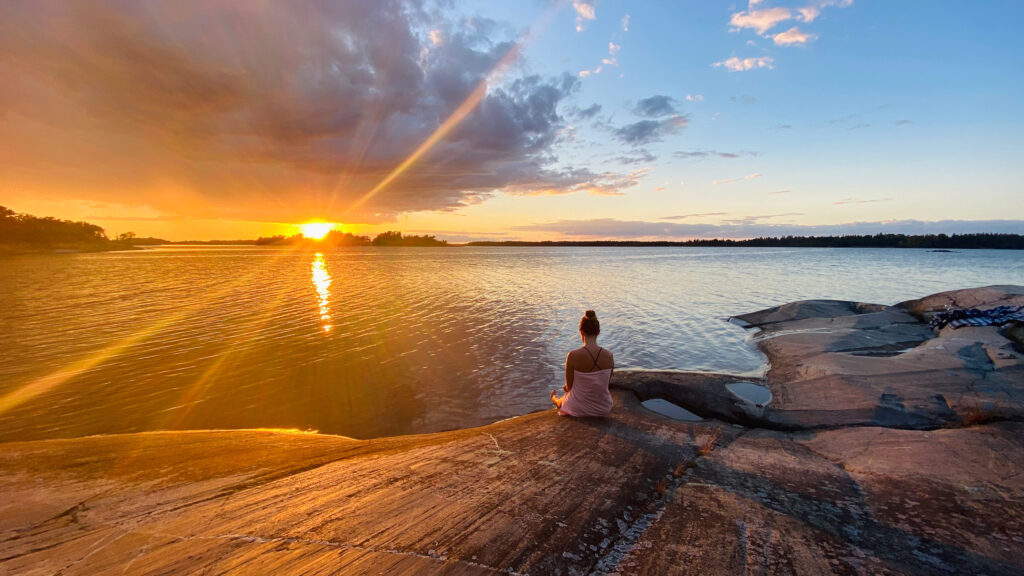 Bild på kvinna som sitter vid vattnet och njuter av solnedgången