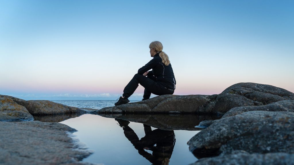 Kvinna sitter på klipporna och njuter av utsikten över vattnet och laddar upp med ny energi